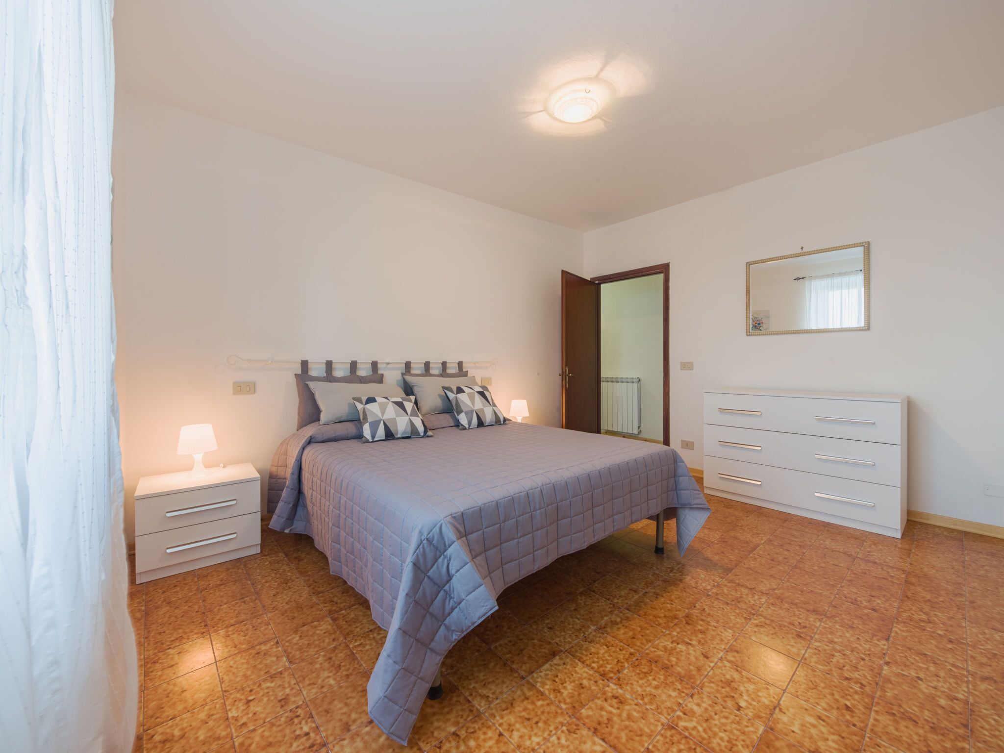 Une chambre à coucher comprenant un lit, des tables de chevet, une commode, un miroir et un luminaire au plafond.