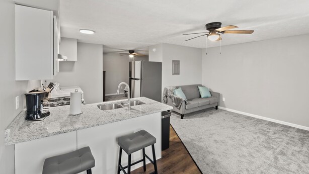 Une cuisine moderne dotée d’un îlot central, d’un coin repas avec un canapé gris et d’un ventilateur de plafond.