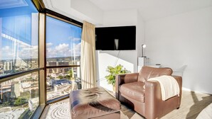 Een moderne woonkamer met een groot raam, een flatscreen-televisie, een leren bank en een klein poufje.