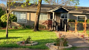 Una casa de un piso con porche delantero, un pequeño jardín y patio cercado.