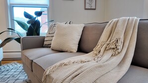 A living room with a beige sofa, a macrame throw, and a striped pillow. - Newly Refreshed 3bd Spacious Unit Minutes from 290 (Worcester)