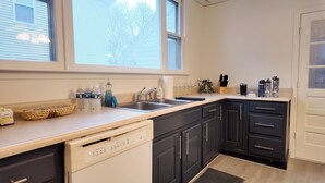 A kitchen with a dishwasher, a sink, and cabinets. There are bottles, a basket, and a plant on the counter. - Newly Refreshed 3bd Spacious Unit Minutes from 290 (Worcester)
