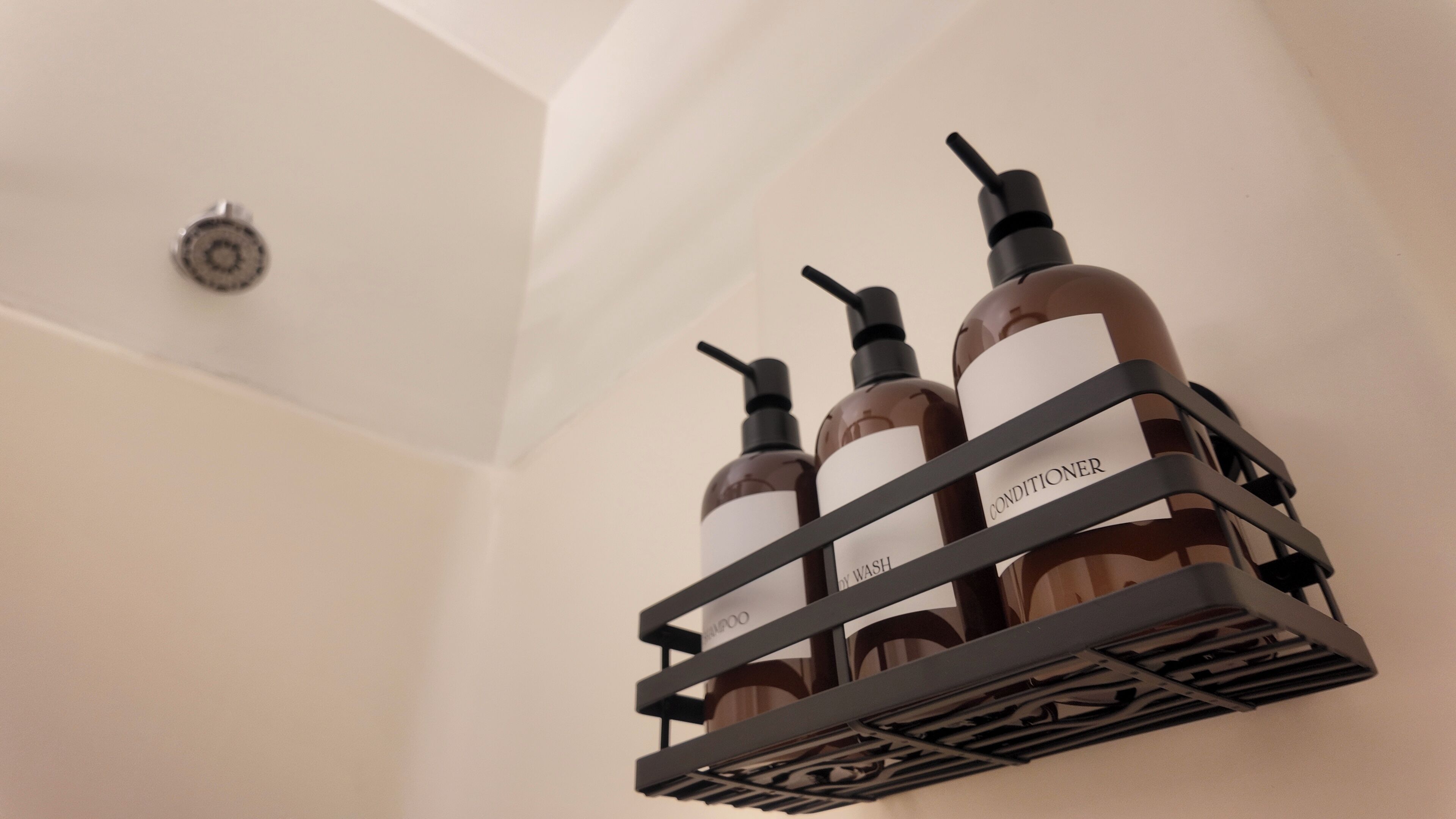Un baño con un estante que contiene tres botellas de champú y acondicionador.