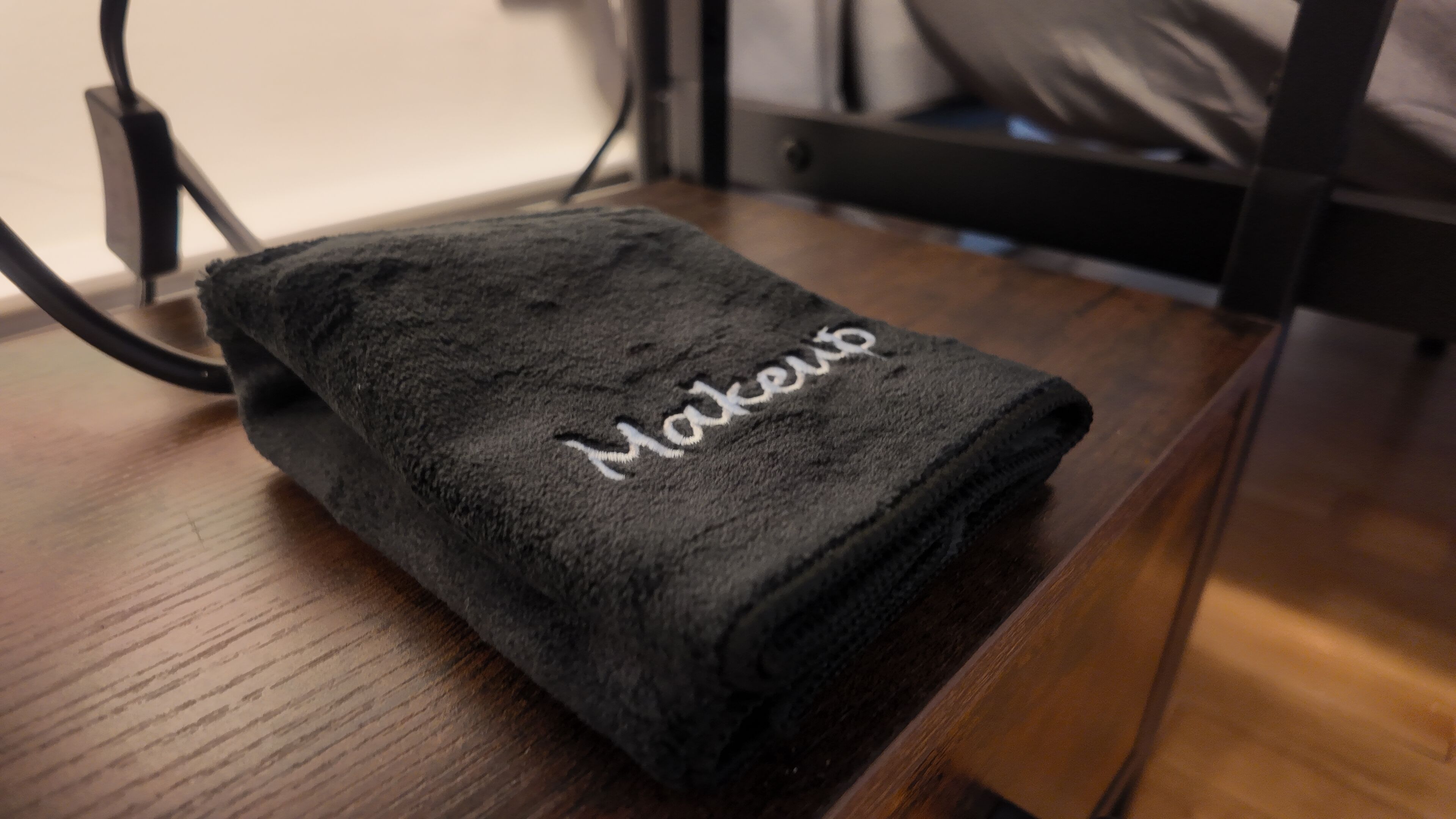 Ein schwarzes Handtuch mit dem Schriftzug 'Makeup' auf einer Holzfläche.