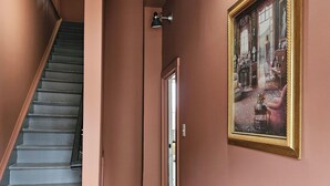 Un pasillo con una escalera, una puerta que da a otra habitación y un cuadro en la pared.