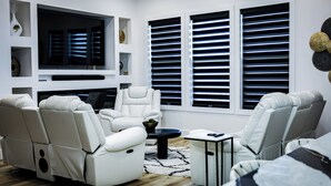 A modern living room with a large flat-screen TV, reclining chairs, a coffee table, and decorative wall shelves. - Charming waterfront 3-bedroom, 3 bath house with gourmet kitchen in Milton, FL (Milton)