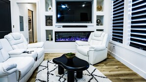 A modern living room with a flat-screen TV, white leather sofas, a black coffee table, and a fireplace with blue flames. - Charming waterfront 3-bedroom, 3 bath house with gourmet kitchen in Milton, FL (Milton)