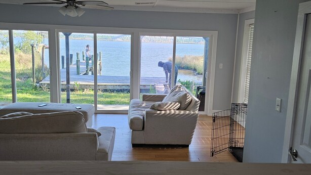 A living room with a large sliding glass door leading to a lake view, a grey sofa, and a wooden floor. - 3-bedroom house in welcoming Moss Point with AC, WiFi (Moss Point)