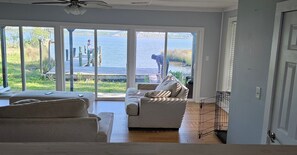 A living room with a large sliding glass door leading to a lake view, a grey sofa, and a wooden floor. - 3-bedroom house in welcoming Moss Point with AC, WiFi (Moss Point)