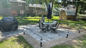 A patio with a table and chairs, surrounded by a gravel border and grass.