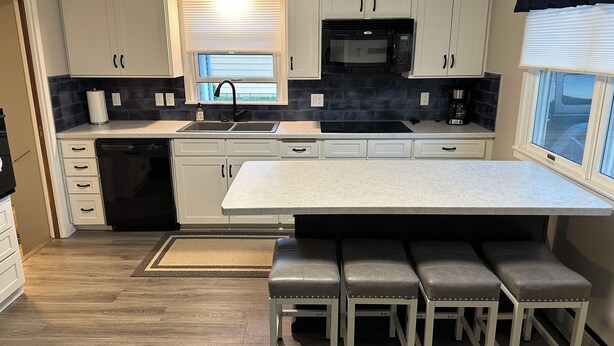 A modern kitchen with white cabinets, a black microwave, a sink, and a large island with bar stools.
