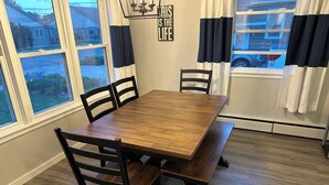 A dining area with a wooden table and chairs, large windows, and a view of the outside.