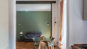 A modern living room with a sofa, a glass dining table, and chairs. - GuestHost - Rione Prati Apartment A (Rome)