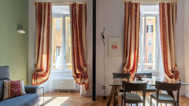 A room with a sofa, dining table, chairs, and curtains. - GuestHost - Rione Prati Apartment A (Rome)
