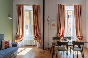 A room with a sofa, dining table, chairs, and curtains.