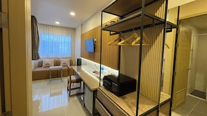 Habitación de hotel moderna con sofá, tocador de madera, escritorio y vestidor con espacio para colgar.