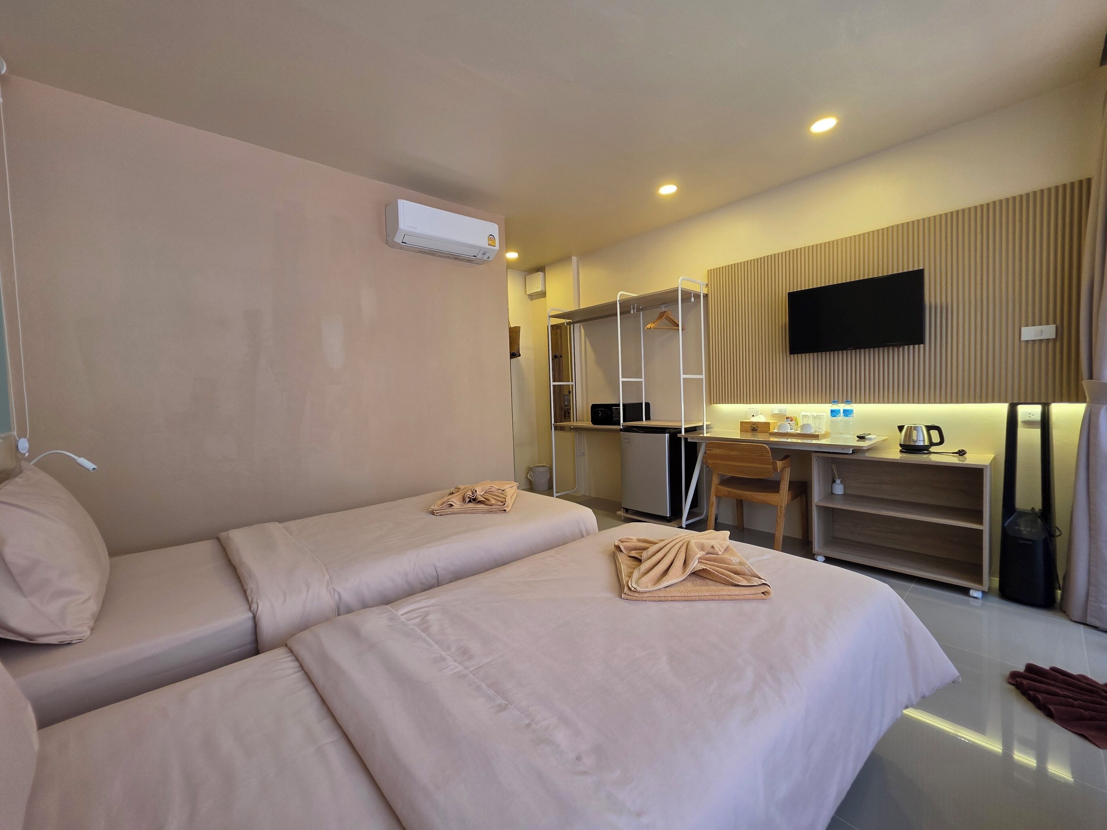 A hotel room with a bed, a desk, a chair, a TV, and a kitchenette.