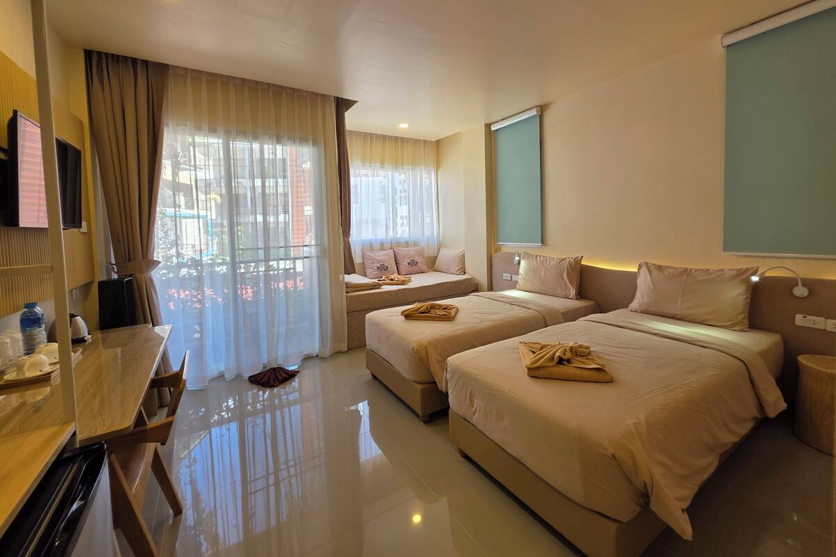 Una habitación de hotel con dos camas, un escritorio, un televisor y una ventana con cortinas.