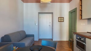 A living room with a sofa, a dining table with chairs, a kitchen area with a stove, and a door leading to another room. - GuestHost - Rione Prati Apartment B (Rome)