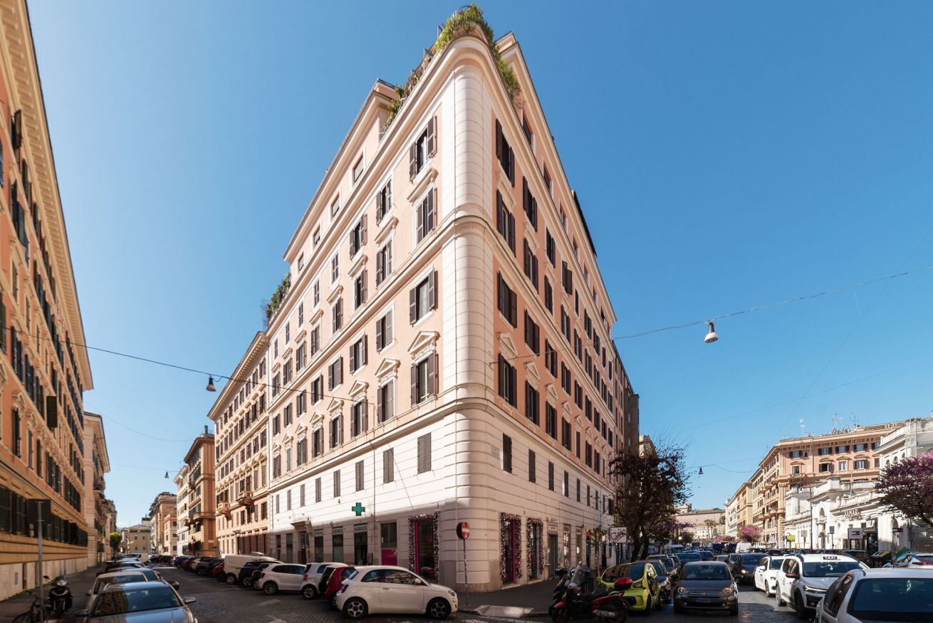 A multi-story building with a corner entrance, parked cars along the street, and a clear blue sky.