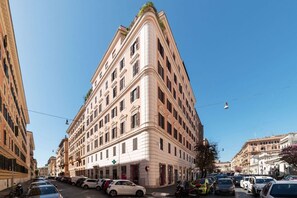 A multi-story building with a corner entrance, parked cars along the street, and a clear blue sky.