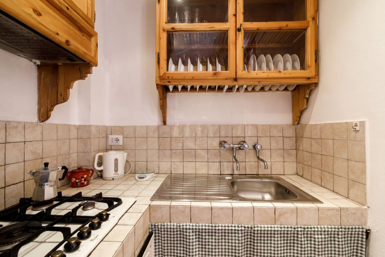 Una cocina con estufa a gas, un lavaplatos, una ventana y platos, además de una toalla de cuadros.
