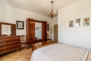 A bedroom with a bed, dresser, mirror, wardrobe, and a chandelier.