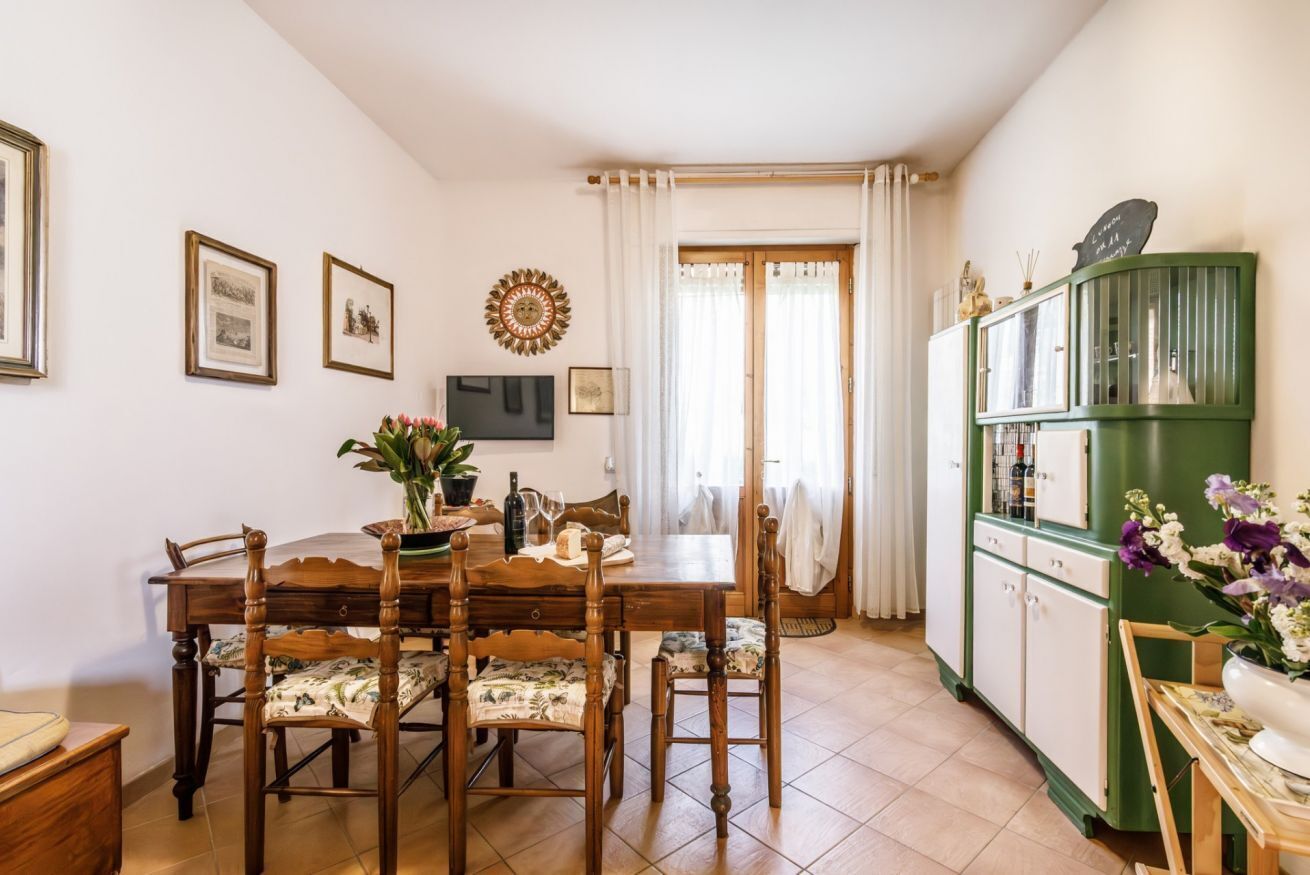 Un comedor con una mesa y sillas de madera, un televisor, cuadros en la pared y un mueble verde con botellas.