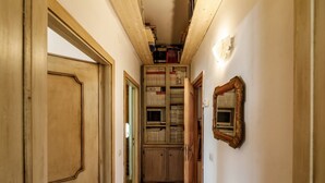 Un corridoio stretto con porte in legno, una libreria a muro e uno specchio.