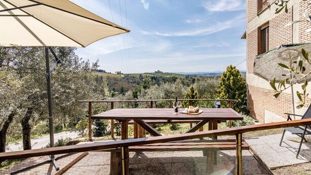 Un patio con tavolo, un bicchiere di vino e pane, con vista su un paesaggio suggestivo.
