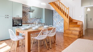 A modern kitchen with a dining table set for four, a wooden staircase, and patterned tile walls.