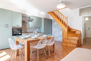 A modern kitchen with a dining table set for four, a wooden staircase, and patterned tile walls.