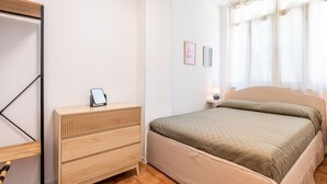 A bedroom with a bed, a bedside table with a lamp, a wooden dresser, and a mirror.