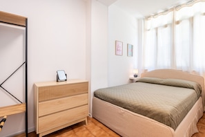 A bedroom with a bed, a bedside table with a lamp, a wooden dresser, and a mirror.