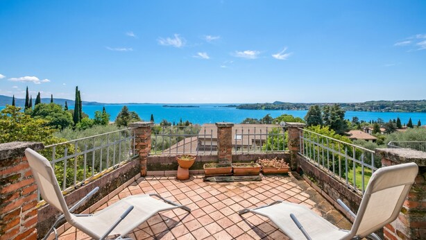A terrace with two white chairs, a brick wall, and a view of a lake.