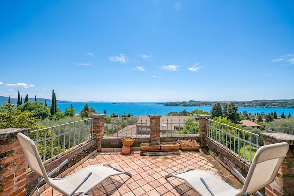 A terrace with two white chairs, a brick wall, and a view of a lake.