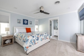 Ein Schlafzimmer mit einem Bett, einem Nachttisch, einem Deckenventilator und einem durch eine offene Tür einsehbaren Badezimmer.