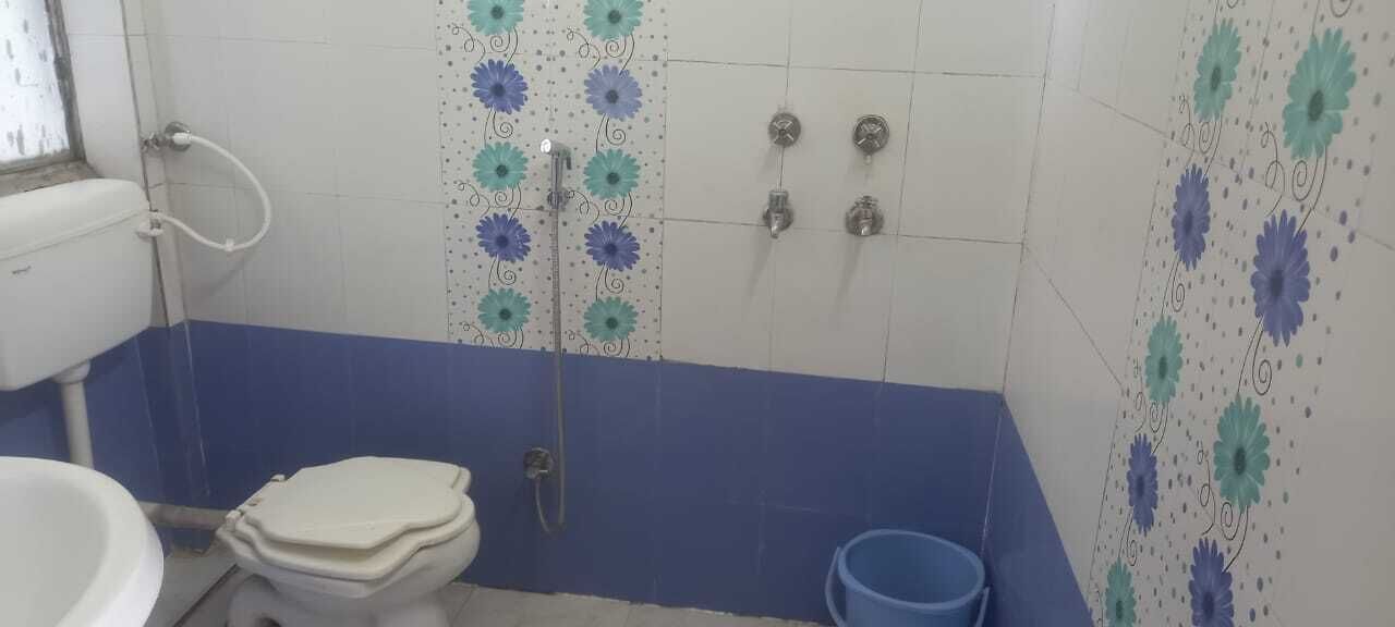 A bathroom with a toilet, shower, and a blue bucket.