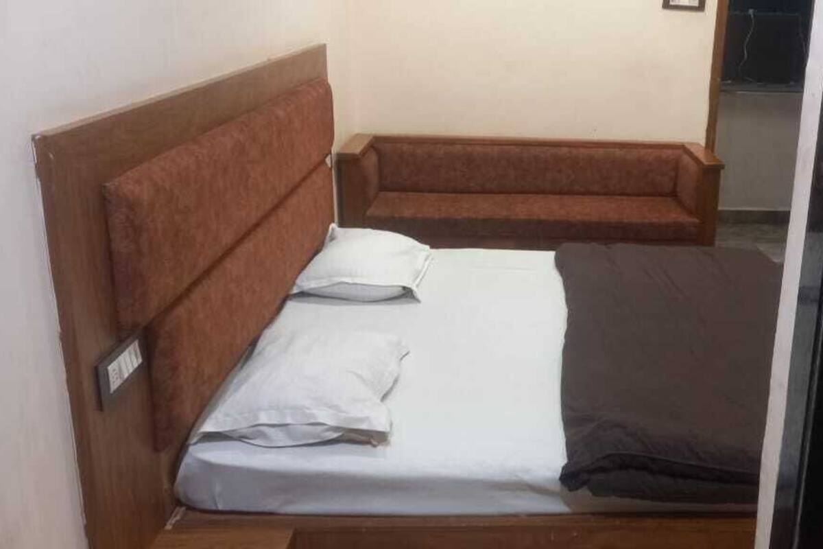 Pieni huone, jossa on yksi sänky, puinen pääty ja ruskea sohva. Lattia on myös puuta.