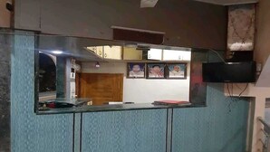 Zona de recepción con mostrador, ventilador de techo, televisor montado en la pared y suelo de baldosas.