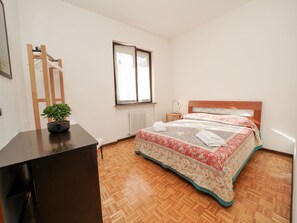 Ein Schlafzimmer mit einem hölzernen Bett, einem Nachttisch, einer kleinen Topfpflanze und einem Fenster mit Vorhängen.