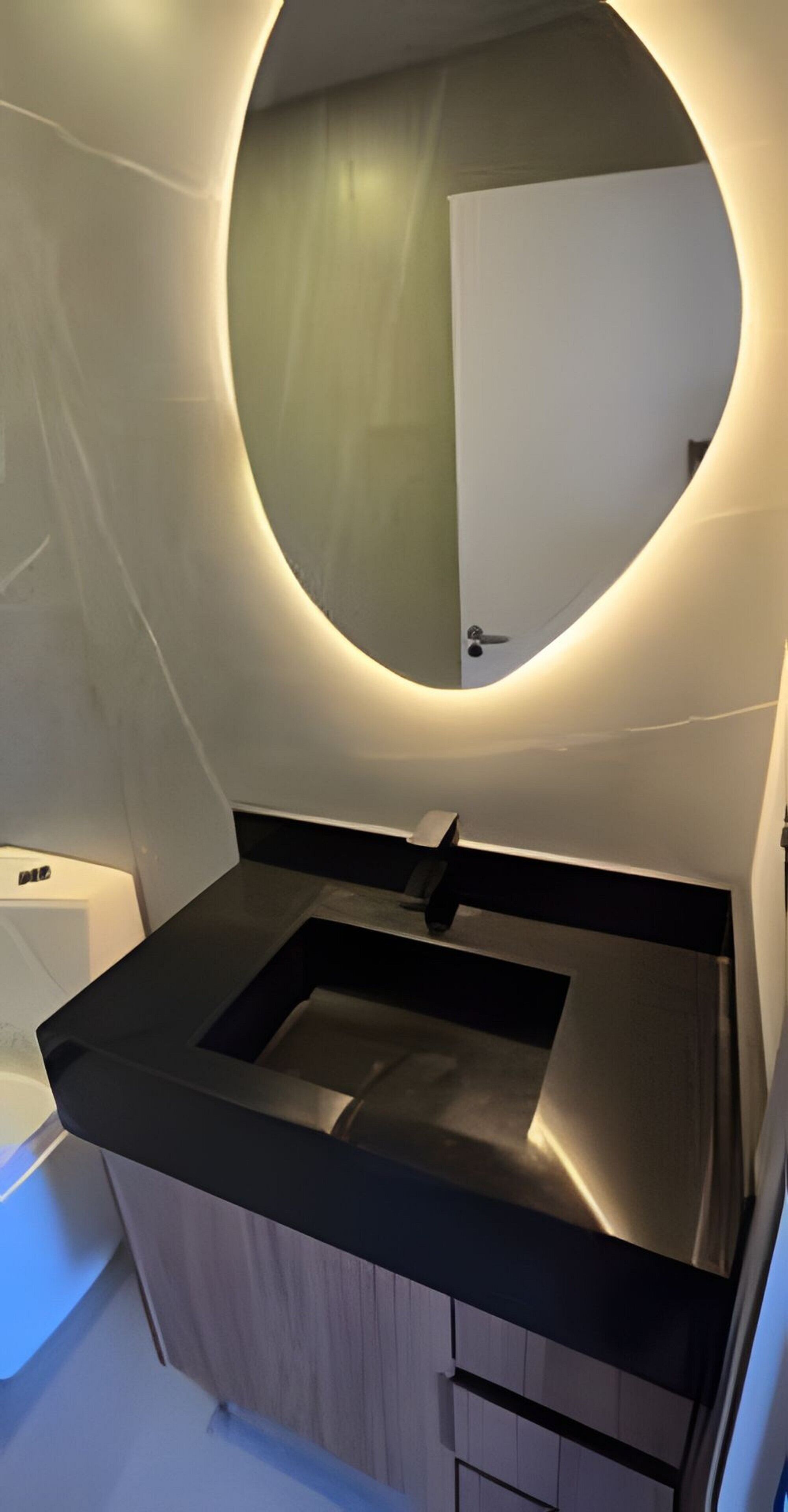 A modern bathroom with a round mirror, a black countertop, and wooden cabinets.