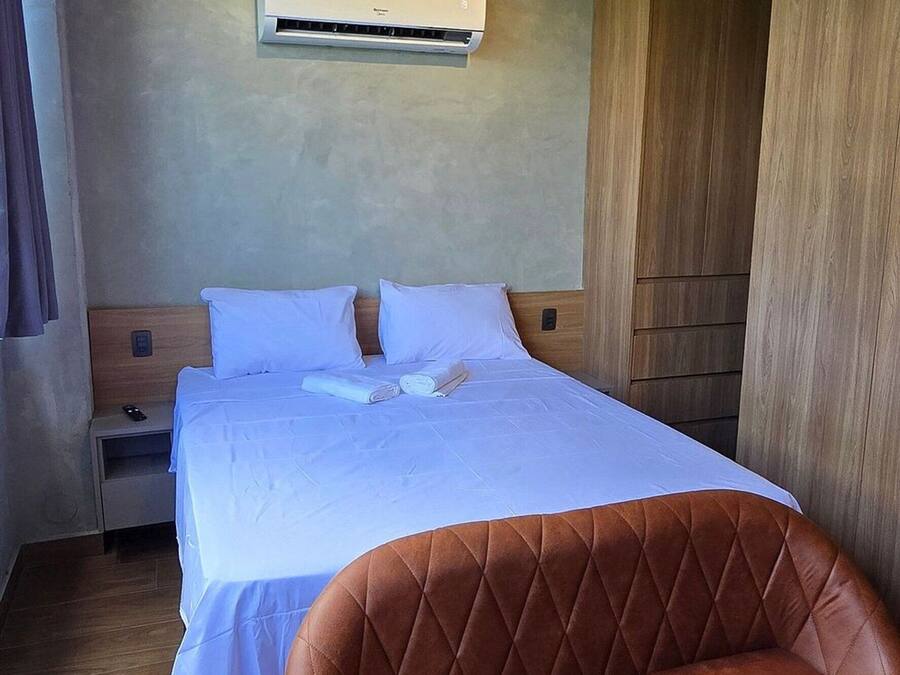 Ein Hotelzimmer mit einem Bett, einem braunen Ledersessel, einem Holzschrank, einem Nachttisch und einer Klimaanlage.
