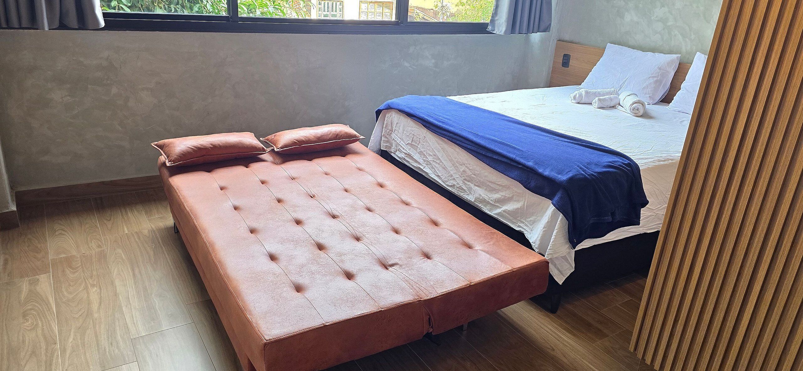 A room with a bed, a bench, and a window.