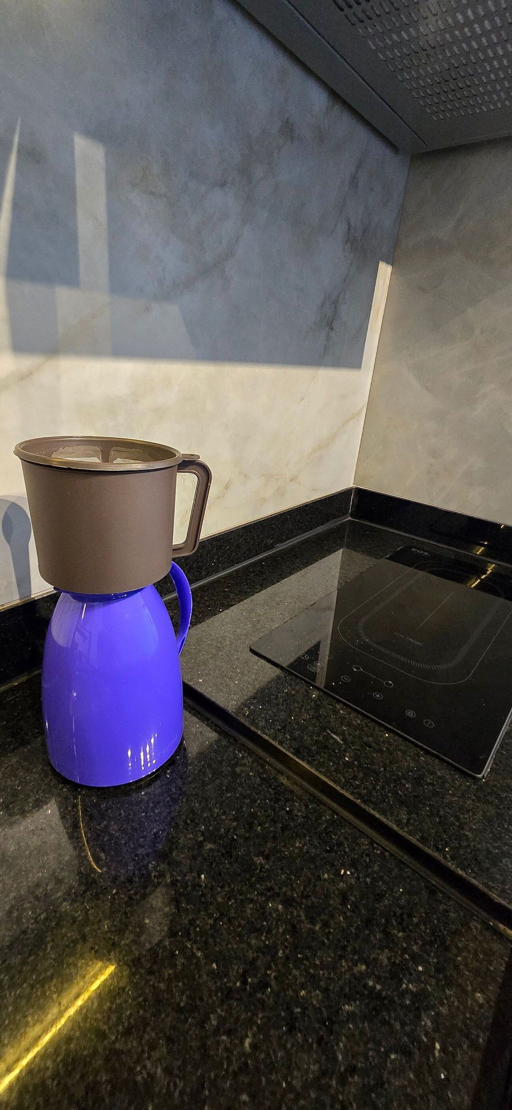 Uma cozinha com uma chaleira elétrica azul sobre uma bancada de granito.