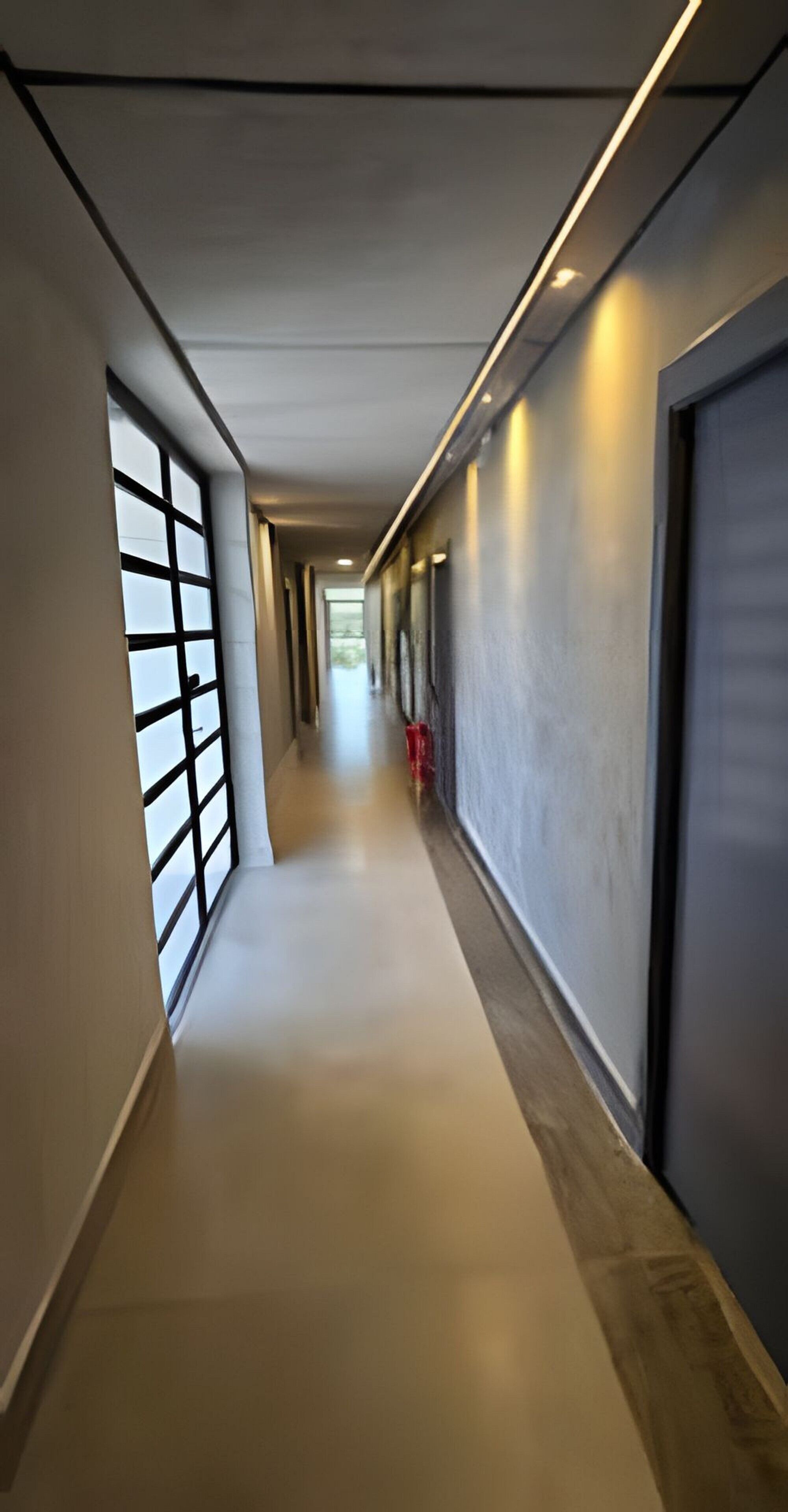 A modern hallway with a light-colored floor, a glass door on the left, and a door on the right.