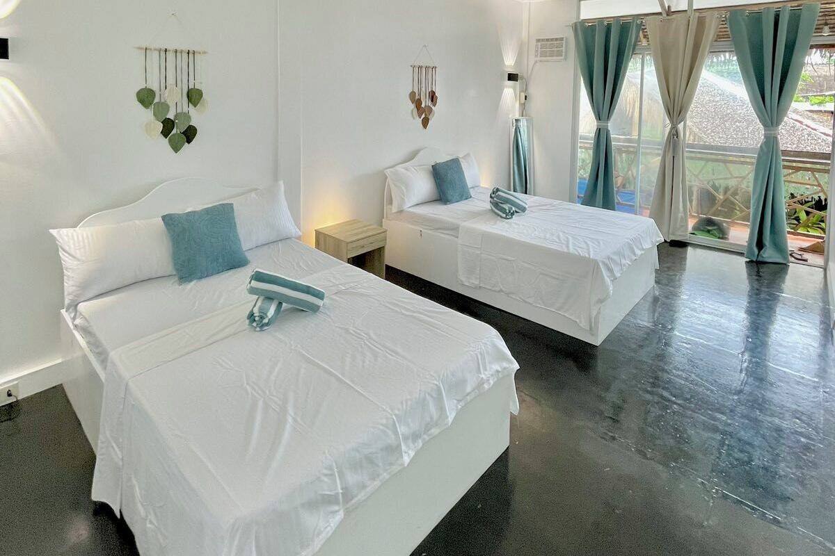 A hotel room with two beds, a large window with curtains, and a wall-mounted light fixture.
