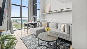 A modern living room with a grey sofa, a round coffee table, and a large window offering a city view. - Senso by Kozystay - Tanjung Barat (Jakarta)