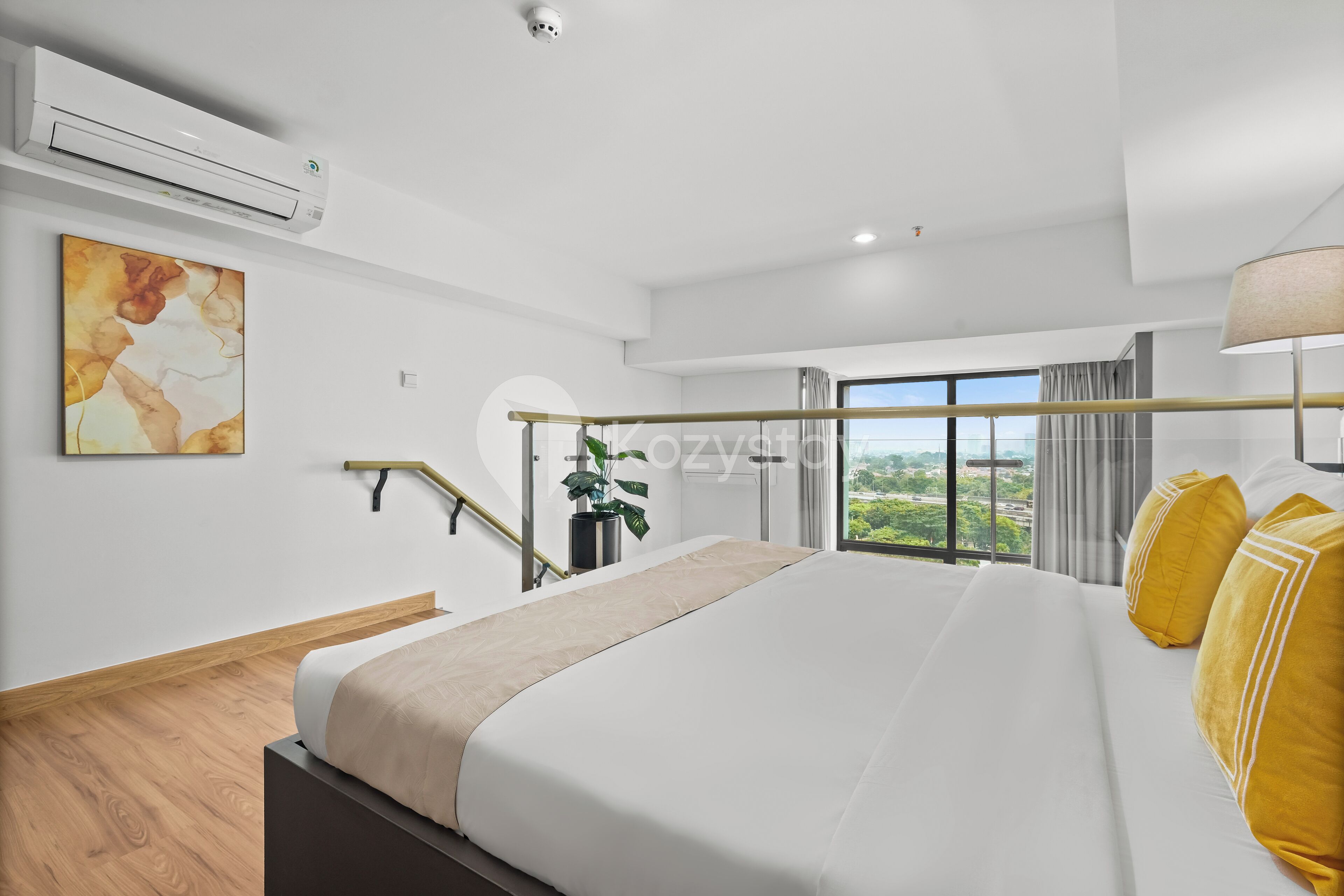 A modern hotel room with a large bed, a view of the outdoors, an air conditioning unit, and a security camera.