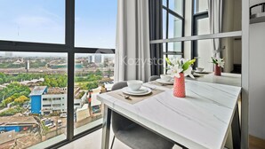 A modern dining area with a large window, a table set with white plates and bowls, and a vase with white flowers. - Senso by Kozystay - Tanjung Barat (Jakarta)